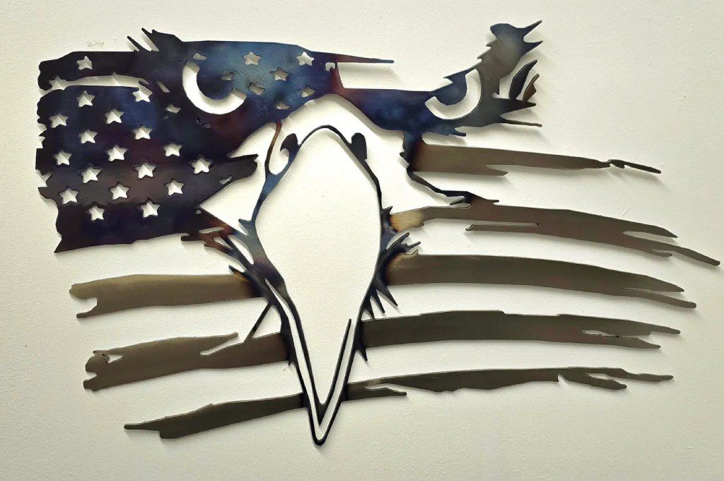 A metal eagle with an american flag in the background.